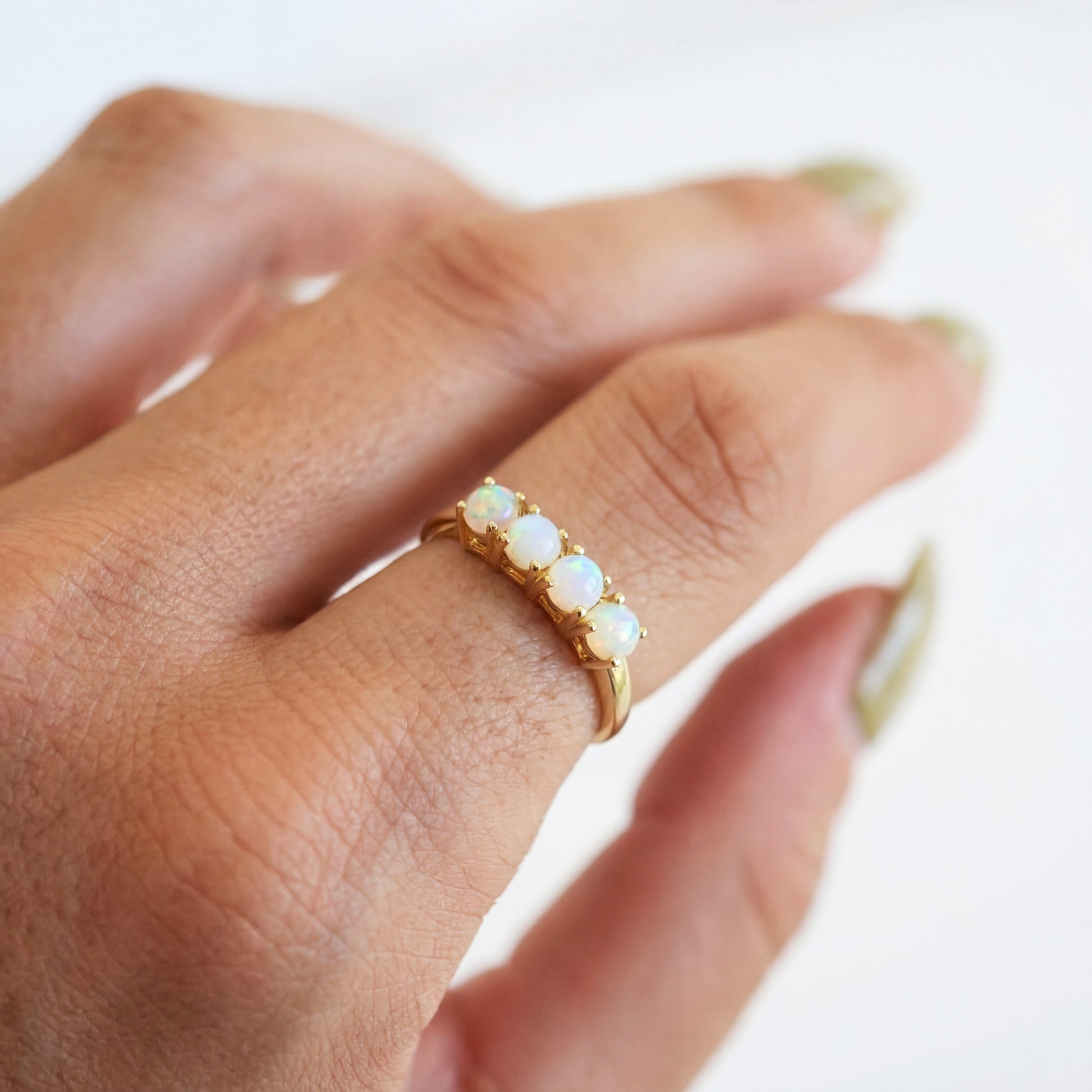 Close-up of a hand wearing a gold ring with opal stones