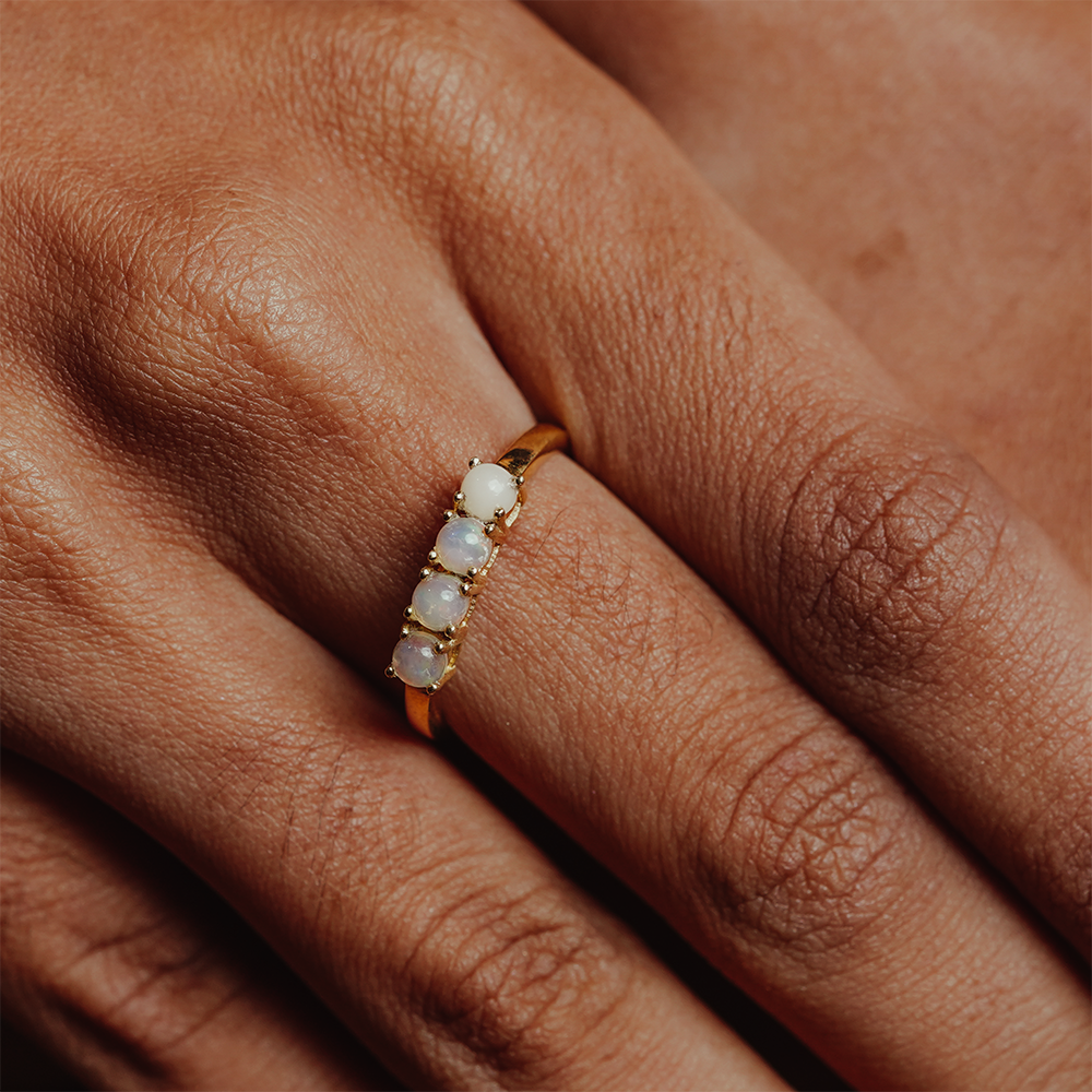 Close-up of a hand wearing a gold ring with opal stones