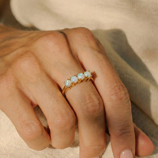 Close-up of a hand wearing a gold ring with opal stones