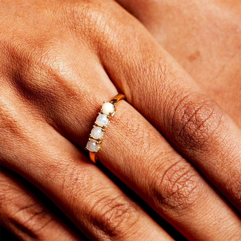 Close-up of a hand wearing a gold ring with opal stones