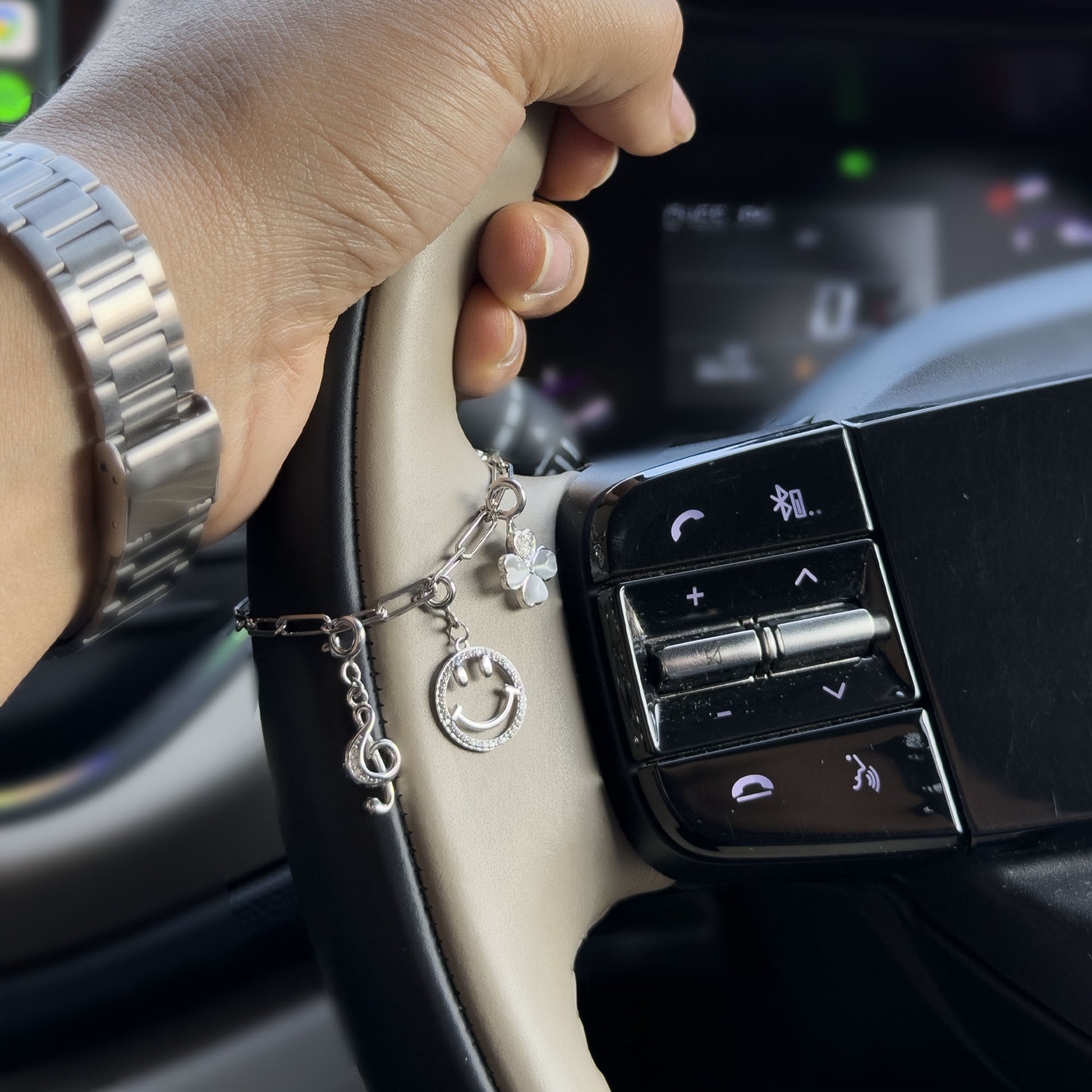 Close up of 925 silver steering wheel charm chain with smiley charm and clover charm on luxury car steering wheel