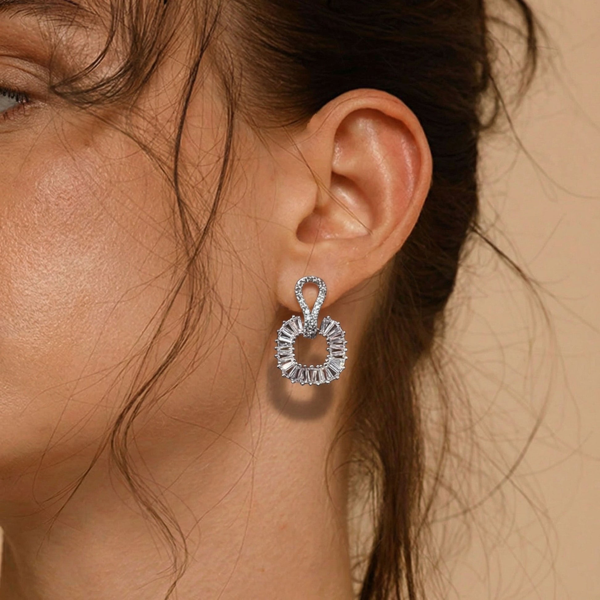 Close-up of a woman's ear wearing a silver earring with a beige background