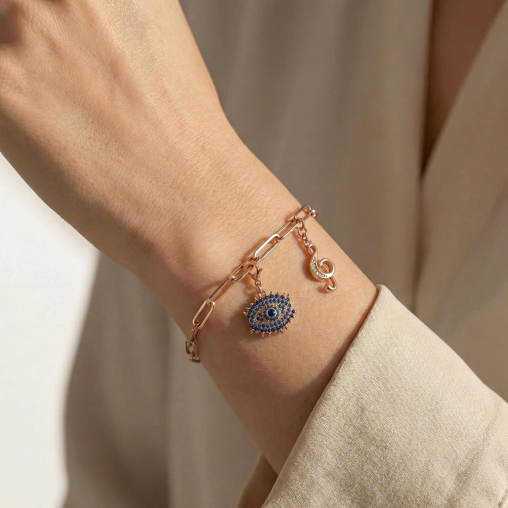 Rose gold paperclip charm bracelet with evil eye charm and clef charm