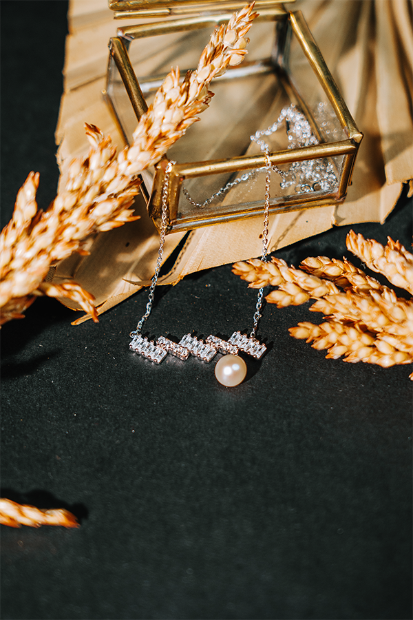 Elfy 925 Sterling Silver geometric necklace for women featuring a modern bar of baguette-cut crystals and a single hanging round pearl. Artistically styled on a dark background with gold accents and wheat stalks—A sophisticated and unique fine jewelry gift 