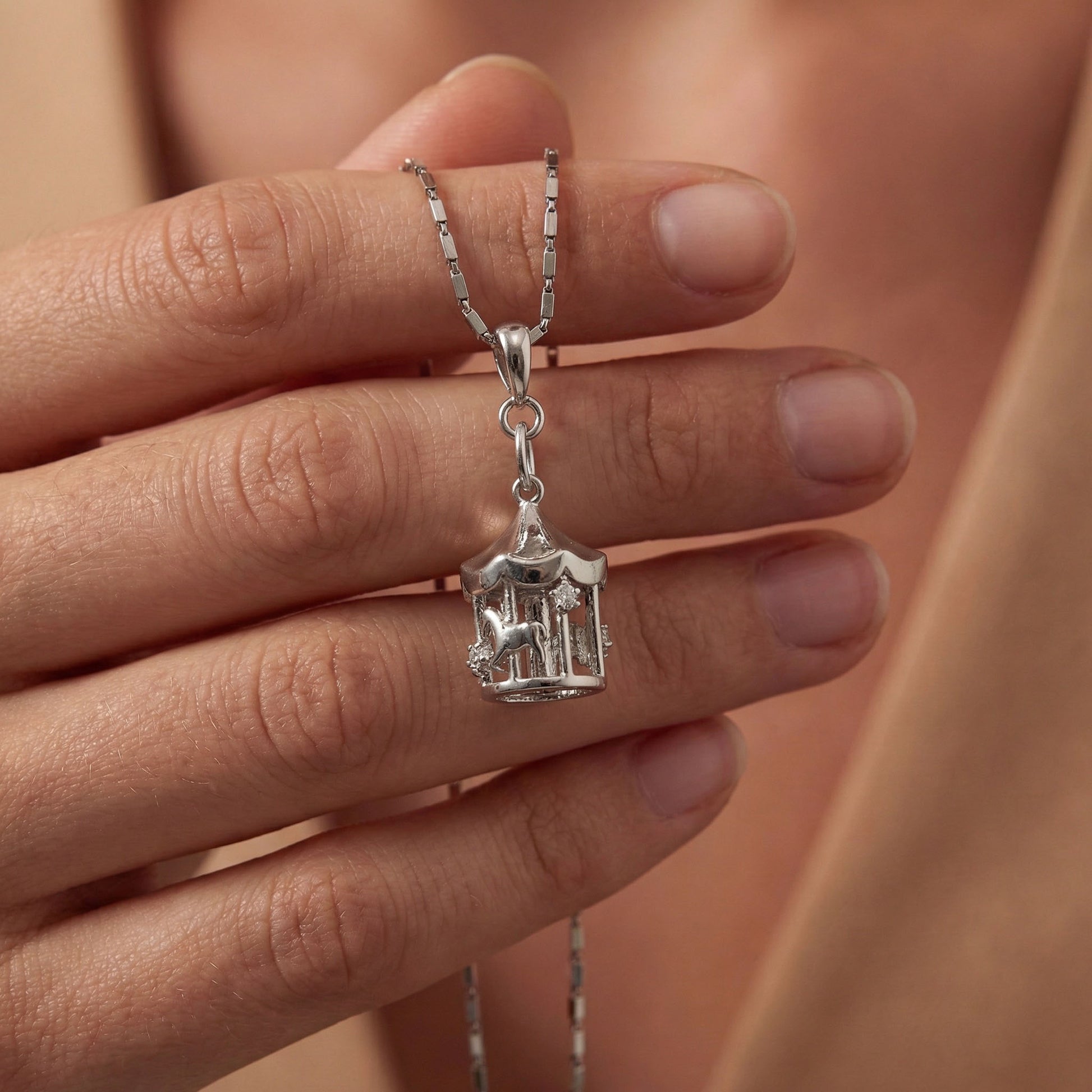 Silver merry go round charm held between fingers, it have horses engraved on it. Merry go round charm, silver charms, sterling silver charms, charm bracelet, charm chain