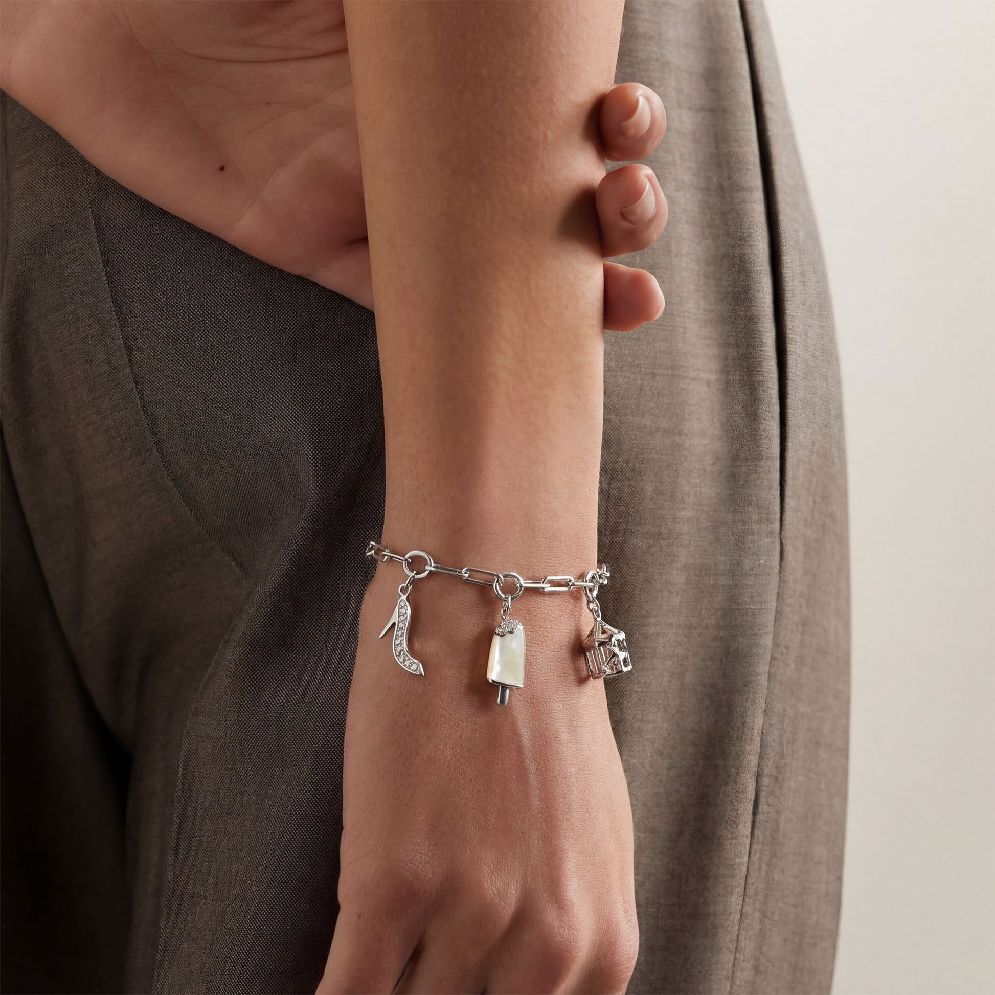 Silver bracelet with charms on a wrist. Charms used are stiletto charm, popsicle or ice cream charm, merry go round charm.