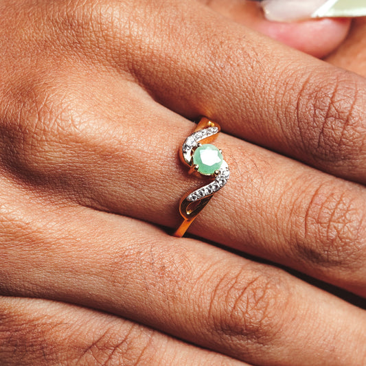 Close-up of a hand wearing a ring with a green gemstone and a flowy pattern