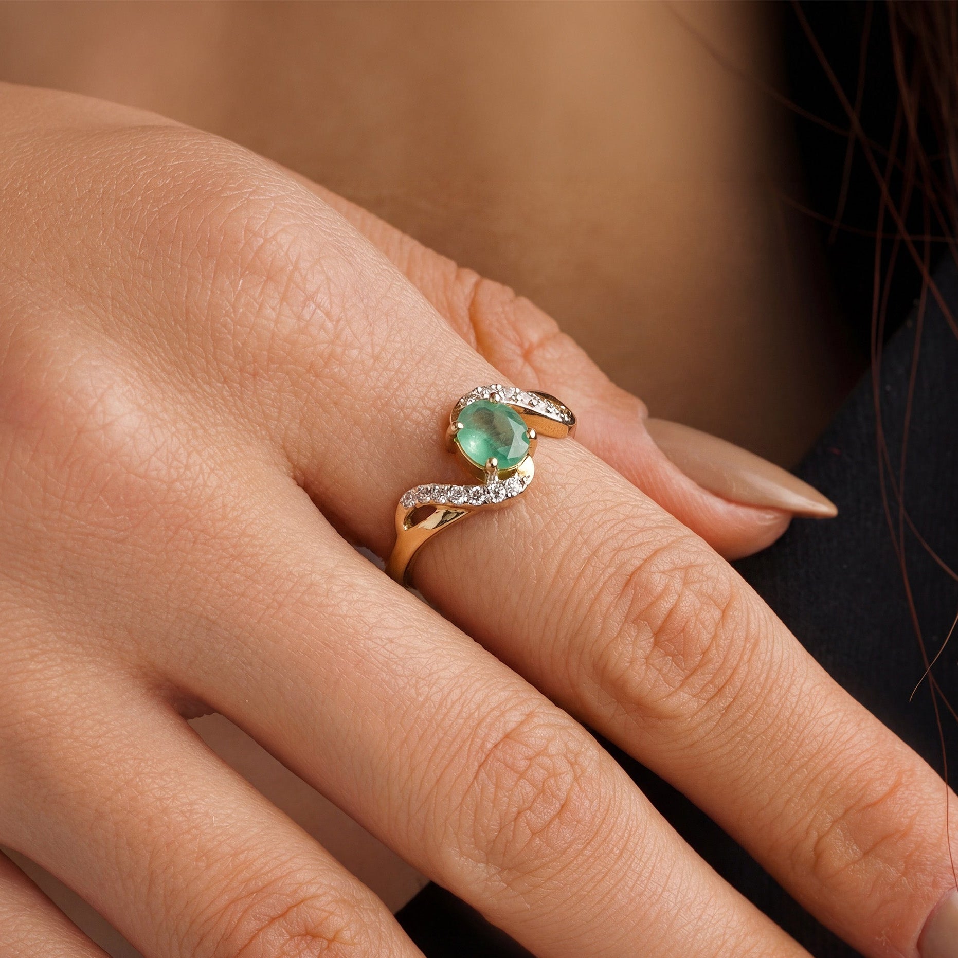 Close-up of a hand wearing a ring with a green gemstone and a flowy pattern