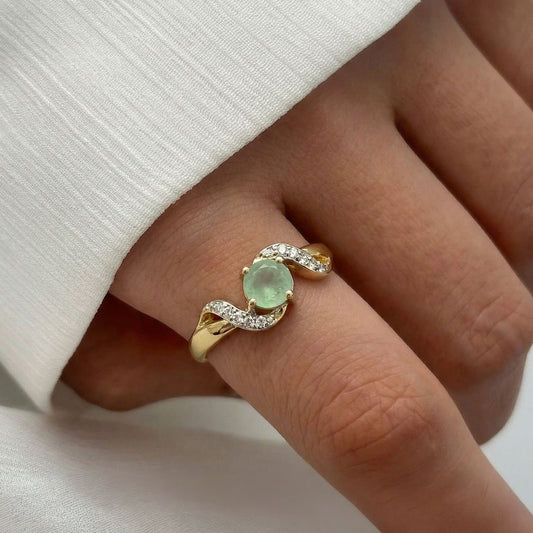 Close-up of a hand wearing a sterling silver gold plated ring with a green gemstone and a flowy pattern