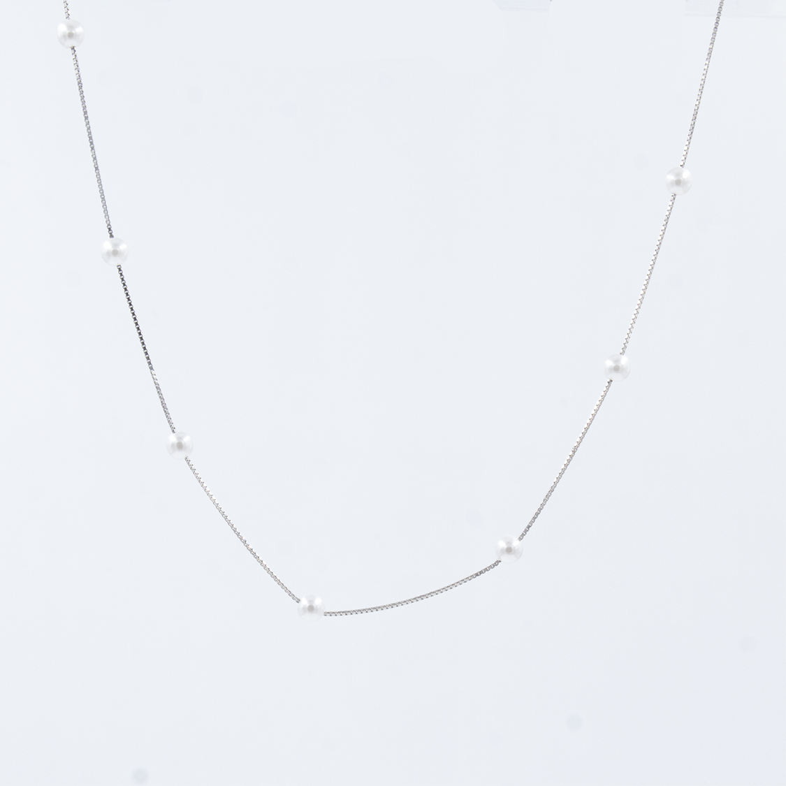A silver pearl chain with a single chain design, featuring spaced out pearls on a white background.