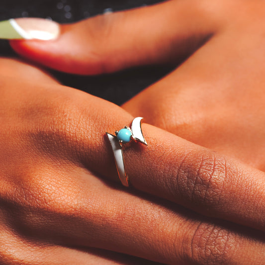 Close-up of a hand wearing a silver ring with a turquoise stone and gold finish