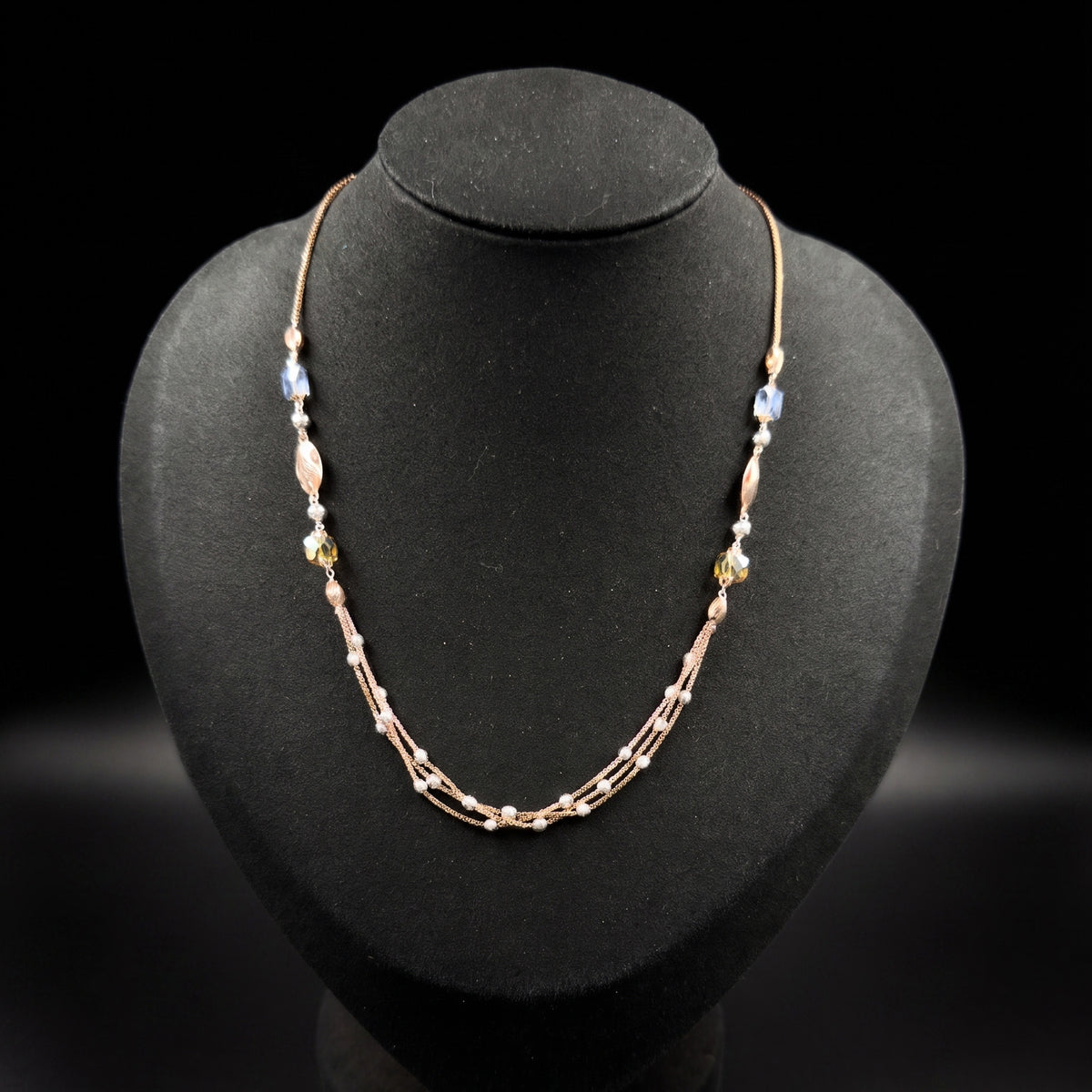 A delicate rose gold beaded necklace displayed on a black jewelry bust against a black background.