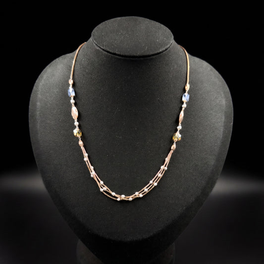 A delicate rose gold beaded necklace displayed on a black jewelry bust against a black background.