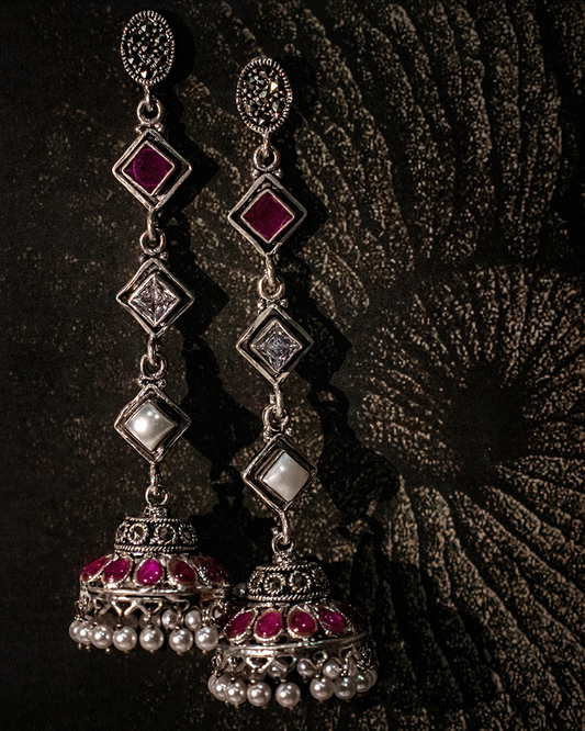 Pair of ornate earrings with red and clear gemstones on a textured dark background