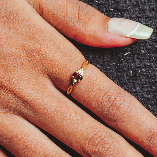Gold ring with a red gemstone on a person's finger against a dark textured background