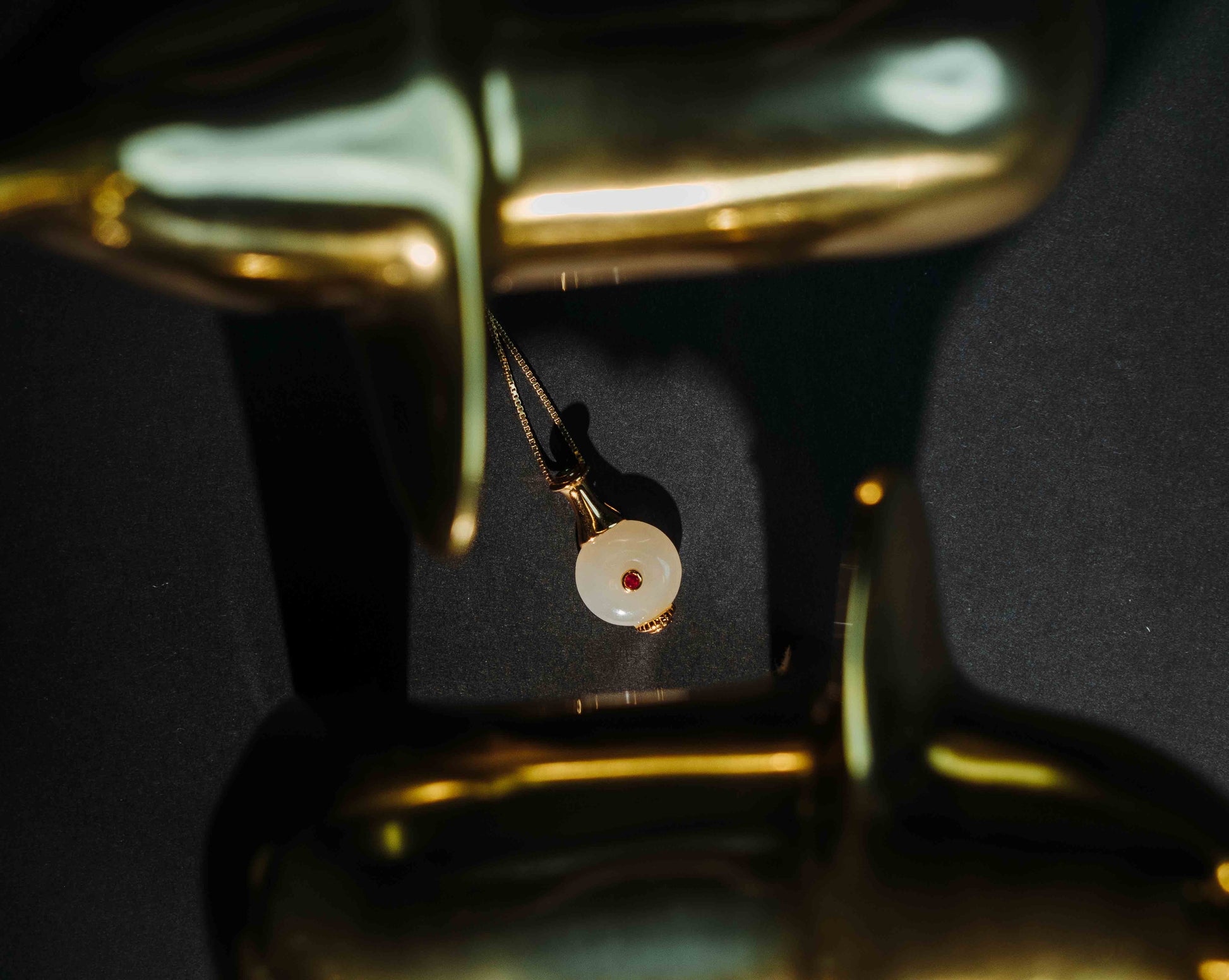 Elfy 925 Sterling Silver gold-plated Royal Vessel Pendant featuring a smooth, milky-white spherical stone with a brilliant red crystal center, artistically framed by golden dolphin figurines on a dark background