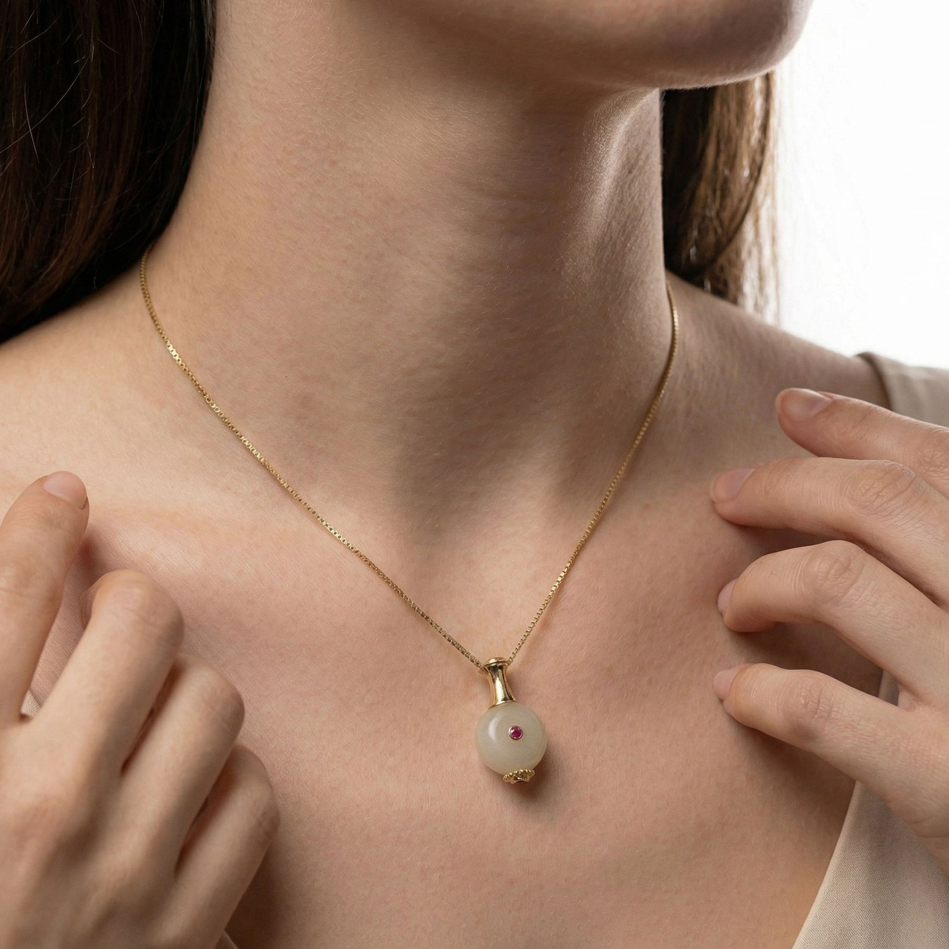 Gold necklace with a bottle shaped pendant worn by a person