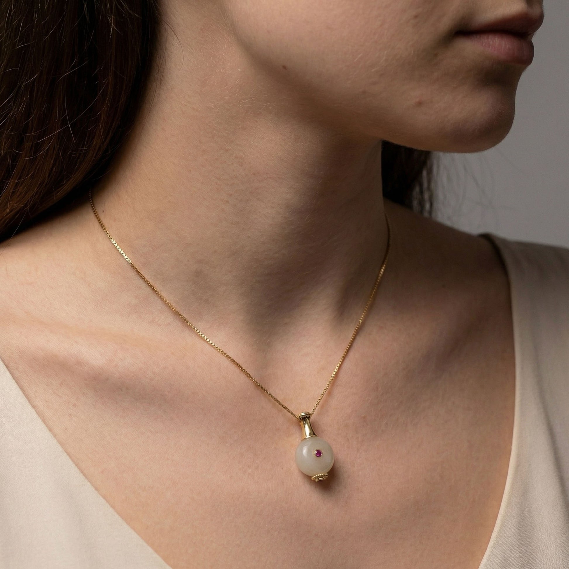 Close-up of a person wearing a gold necklace with a pearl bottle pendant.