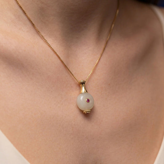 Silver gold plated pendant with a pendant featuring a pearl and red gemstone on a person's neck.