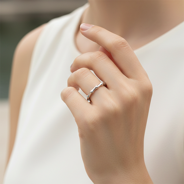 Close-up of a hand wearing a silver Bamboo design ring with a blurred background