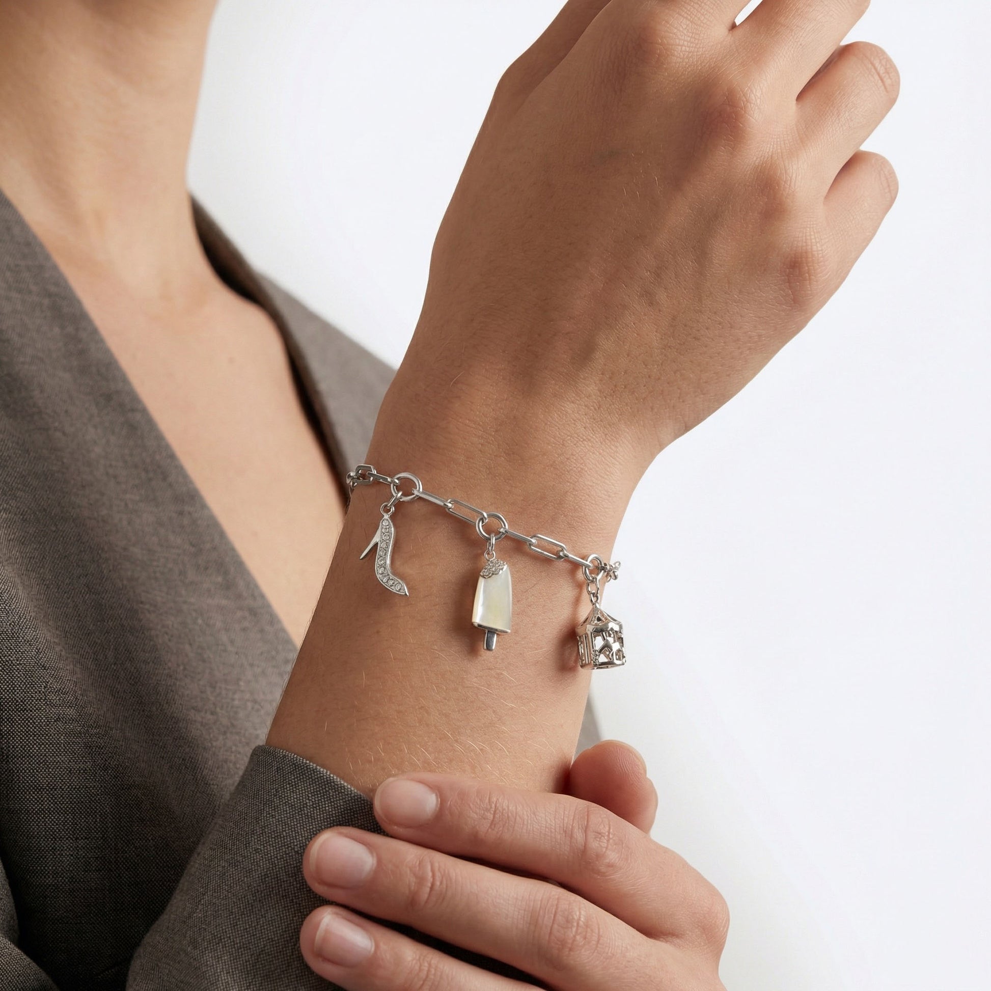 Silver charm bracelet on a wrist. Bracelet is in silver with rhodium plating. the charms are stiletto charm, ice cream charm and merry go round charm.