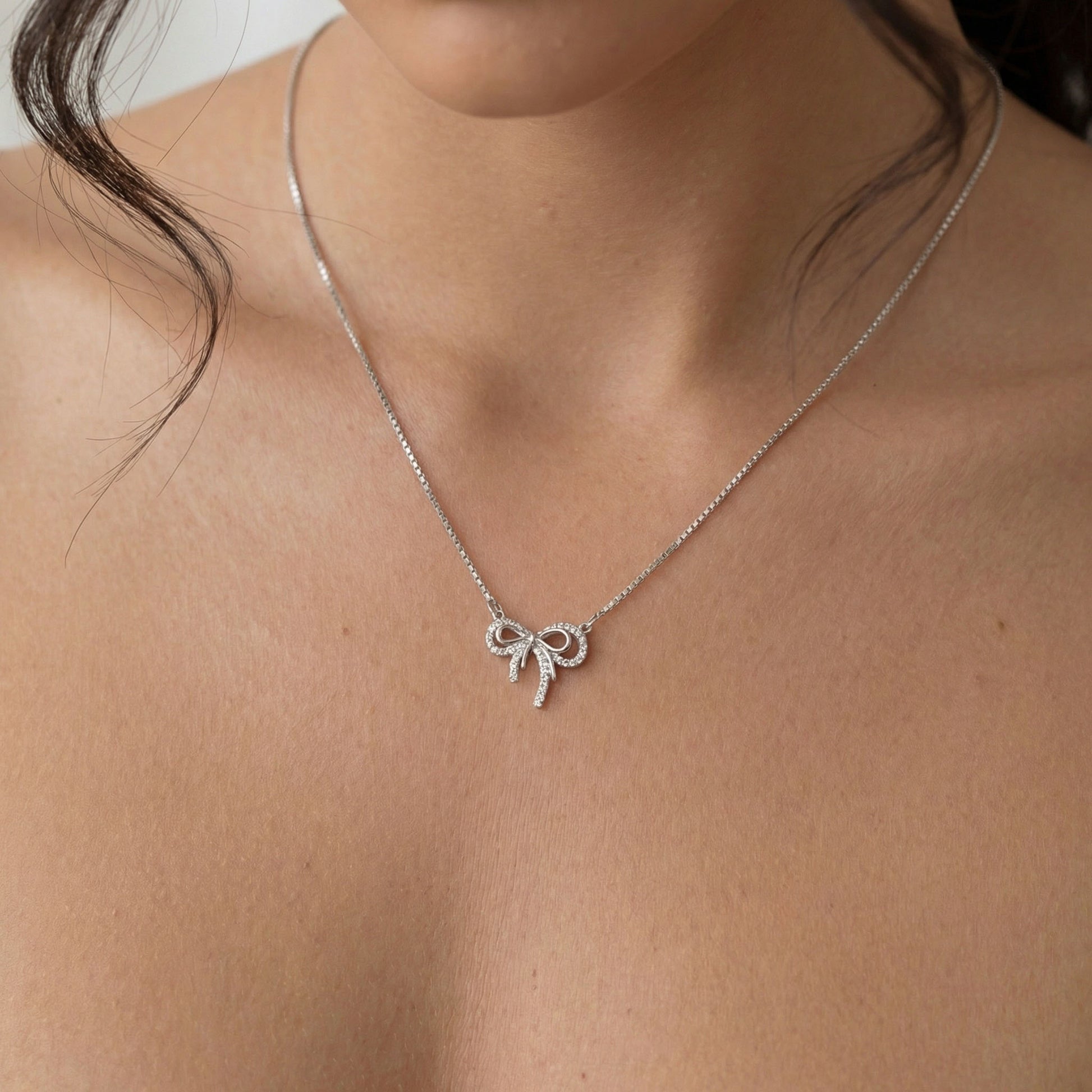 Silver necklace with a bow pendant on a person's neck