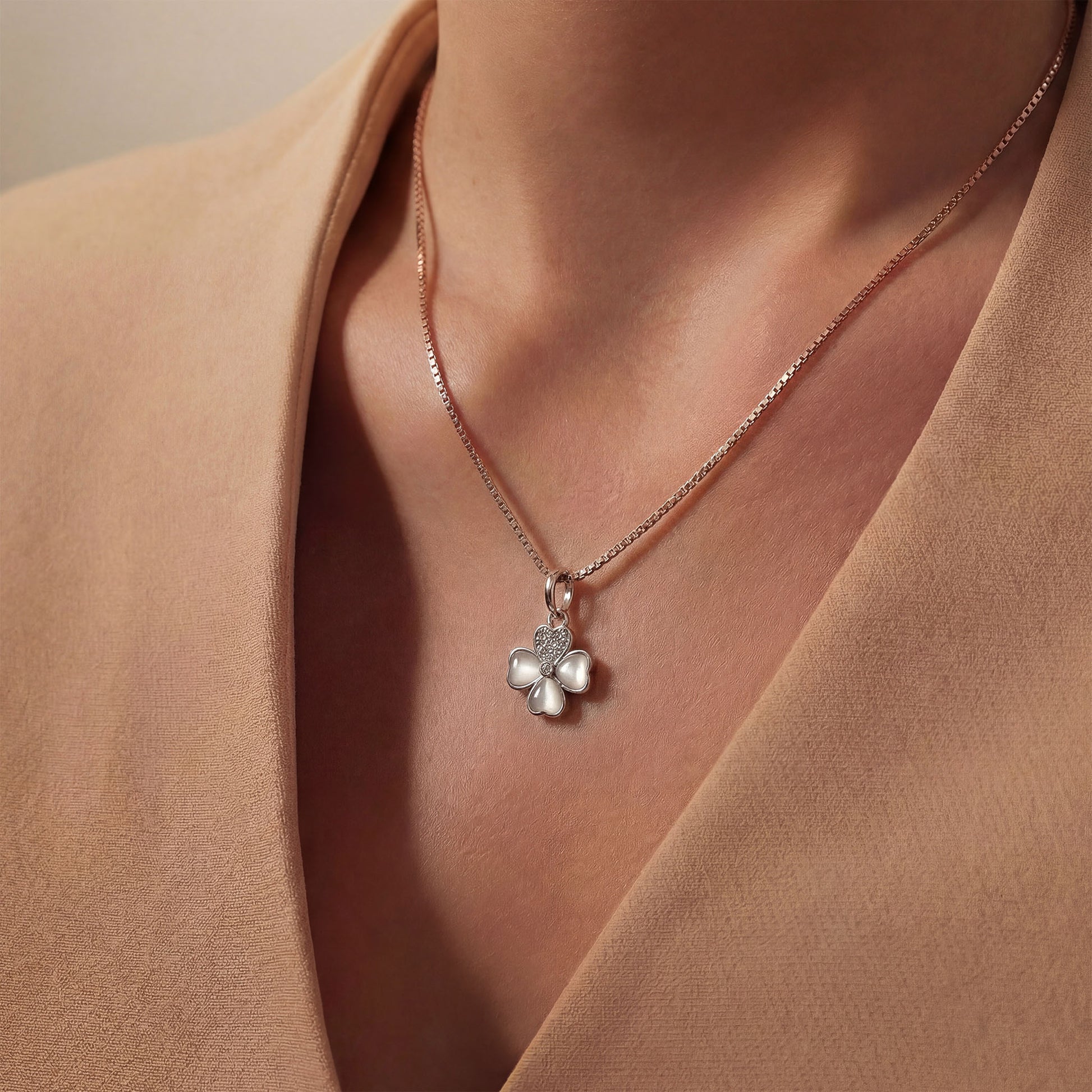 Silver chain with a clover charm worn by a person in beige outfit.