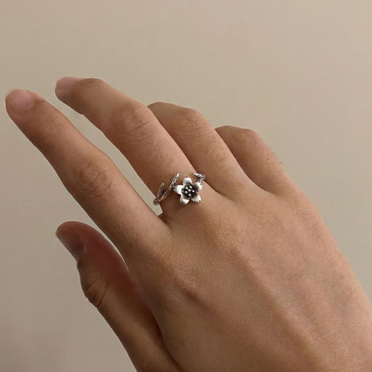Hand wearing a silver ring with a floral design on a plain background