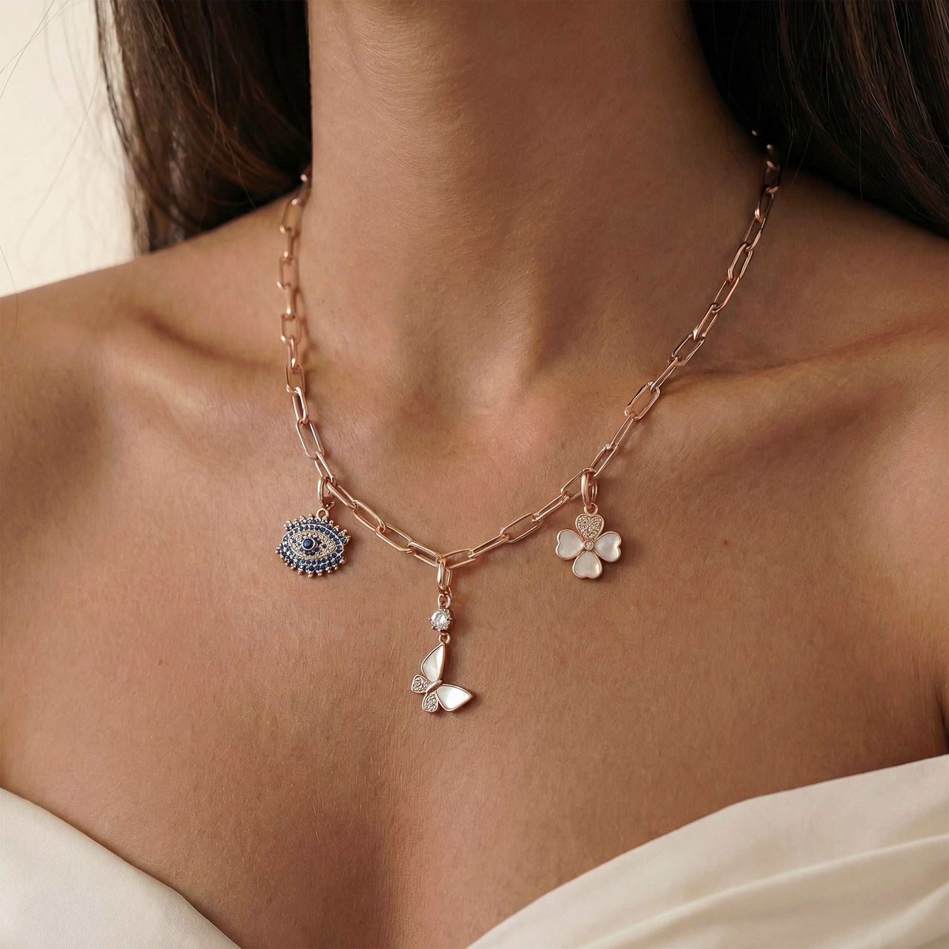 Paperclip charm chain with various charms including an evil eye, flower, and butterfly on a person's neck. all in rose gold chain and all charms are rose gold